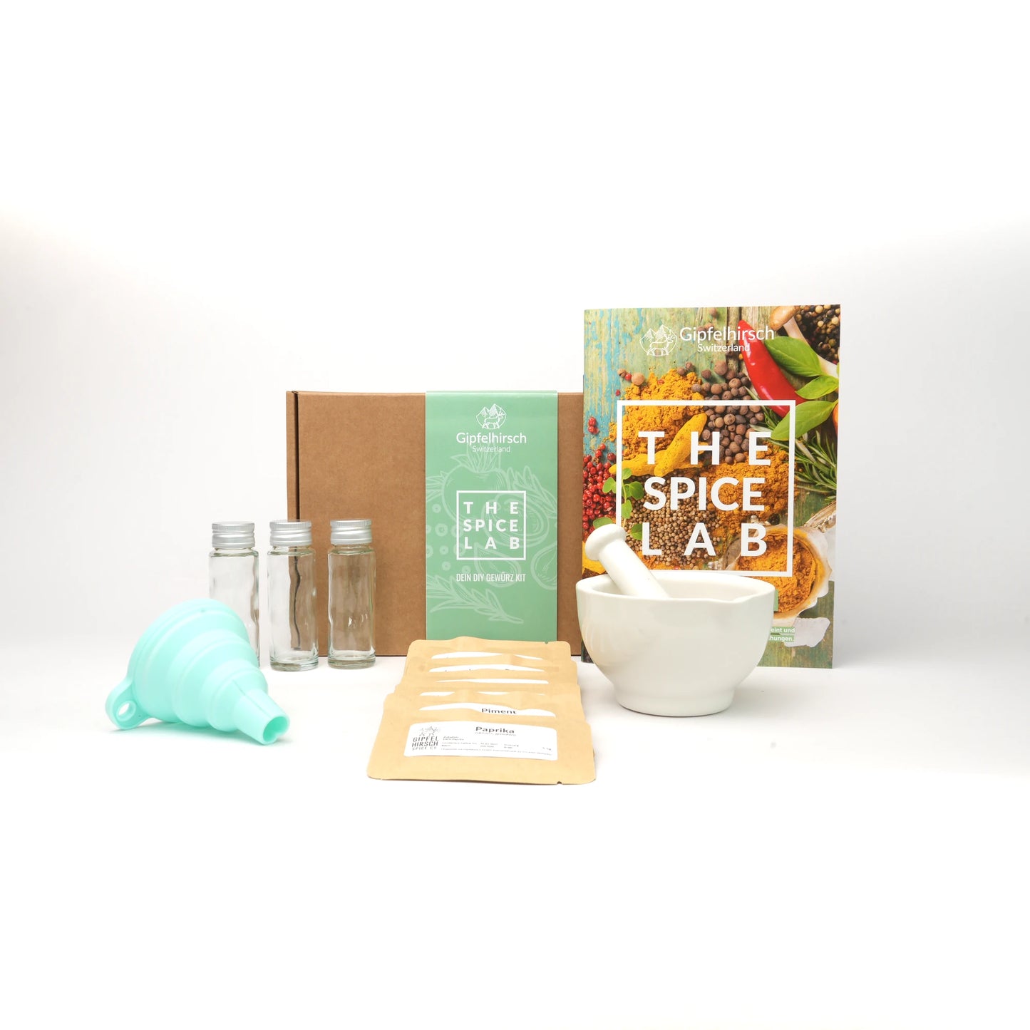 Collection of the content of the spice lab kit including a box, spices, funnel, bottles, a mortar and pestle, and a book titled 'The Spice Lab' on a white background.