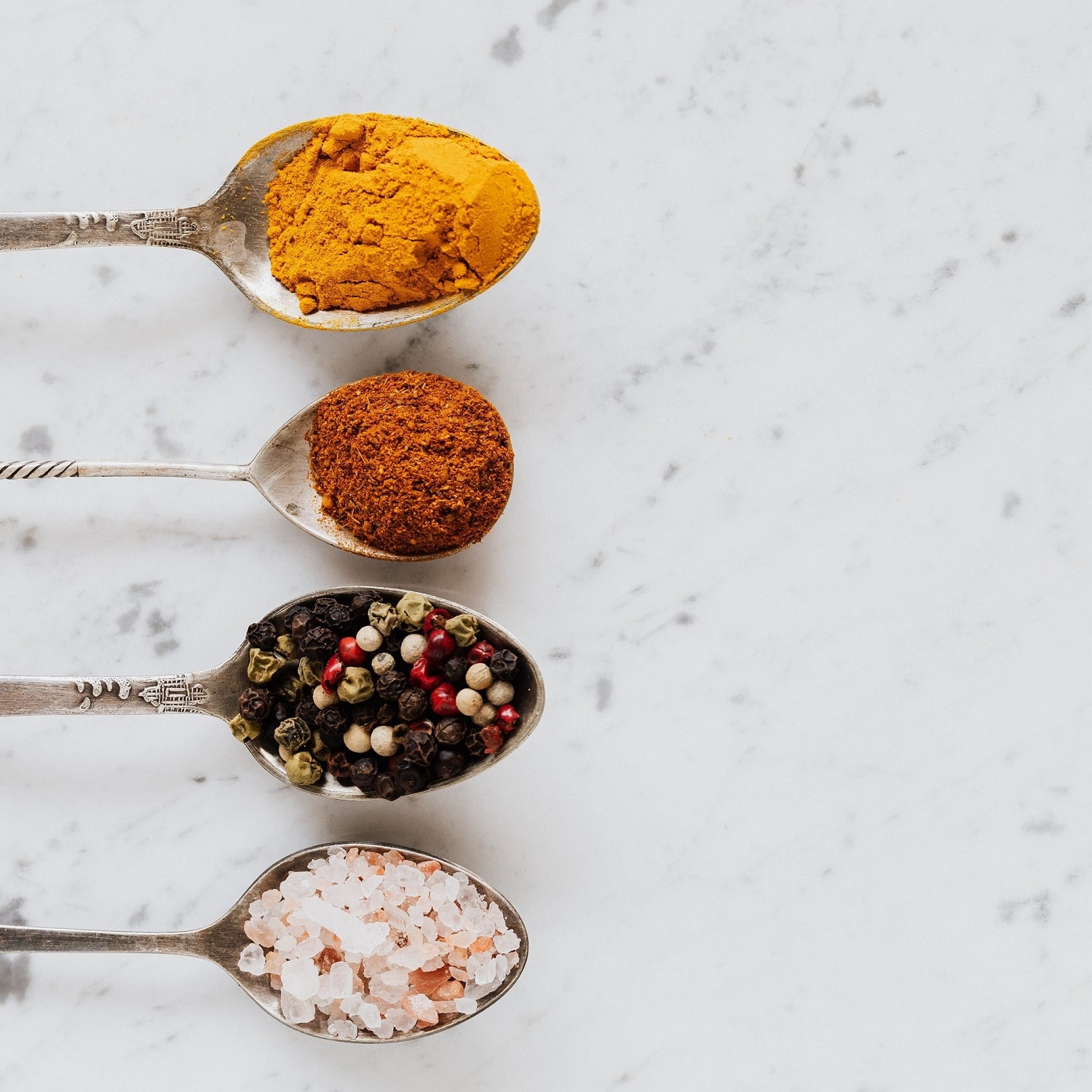 rustic spoons filled with pure spices, such as paprika, salt flakes and peppercorns, put on a marble table in a clean layout